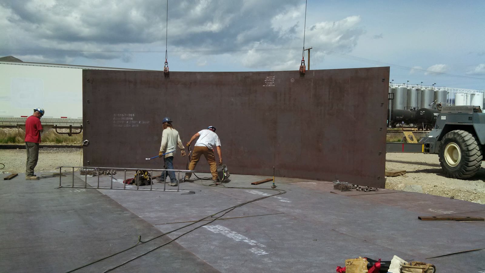 Two welders fabricating a large curved steel tank panel on site in Utah.