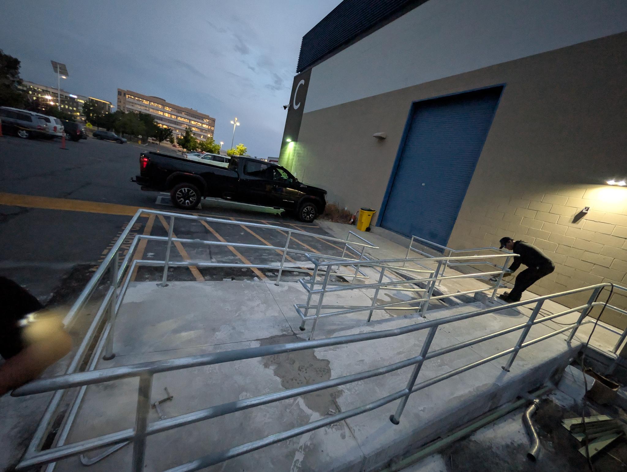 Galvanized ramp railings installed outside a commercial building at dusk.