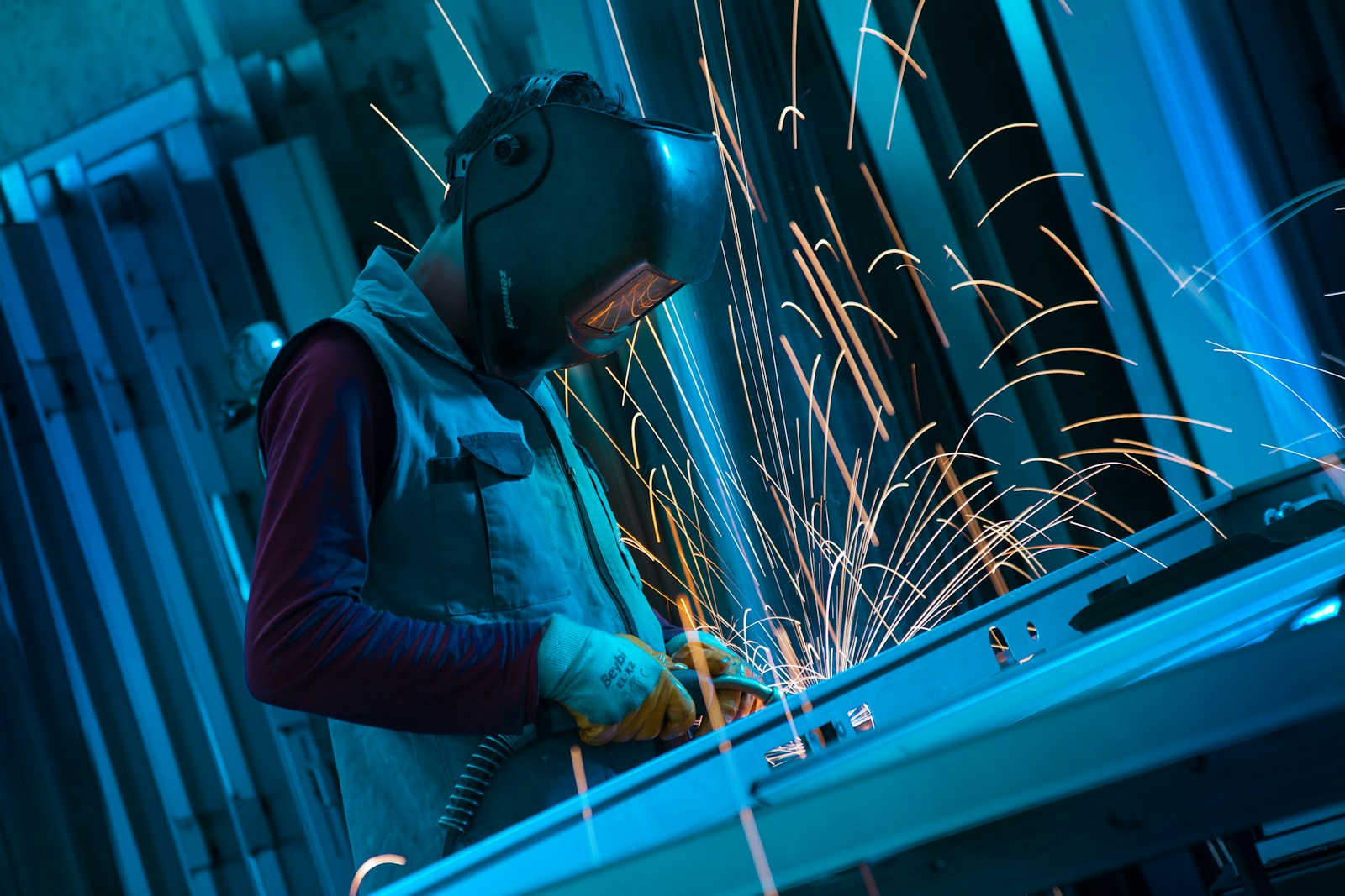 A welder in a mask running a bead on a steel frame with blue and orange light around them.